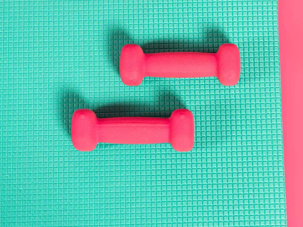 A pair of pink dumbbells resting on a teal fitness mat