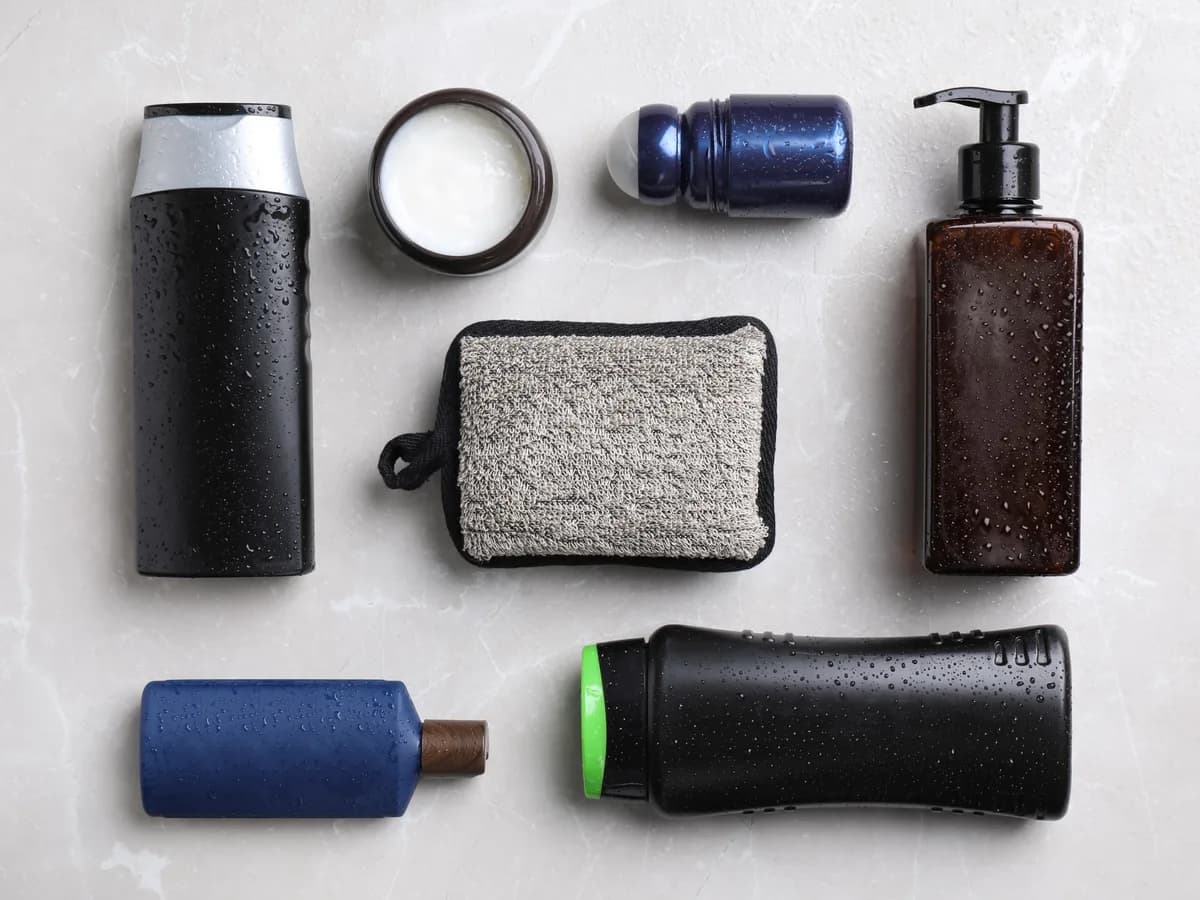 Flat lay of men's grooming products including body wash, moisturizer, deodorant and beard oil on a marble surface